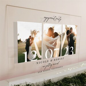 K&ouml;nnte beinhalten: Ein rechteckiges Schild aus klarem Acryl mit drei vertikalen Fotopaneelen eines Paares. Der Text lautet engagement party, 12 07 23, NICOLE & ROBERT are getting married und SAN DIEGO, CALIFORNIA. Das Design enth&auml;lt einen sanften Farbverlauf.