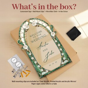 May include: A rectangular wedding sign with an arched top, featuring a green and gold stained glass-style border with white roses. The text reads: Welcome to our wedding, Amelia and John, 10.15.25. Includes wall mount clips, screws, and a cloth.