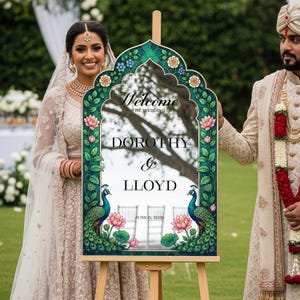 Op de afbeelding: Een trouw welkomstbord op een houten ezel met een boogvormig frame, groene randen, bloemmotieven en twee pauwen. De tekst luidt: Welcome to the wedding of Dorothy & Lloyd, June 6, 2026. Het bord heeft een reflecterend oppervlak.