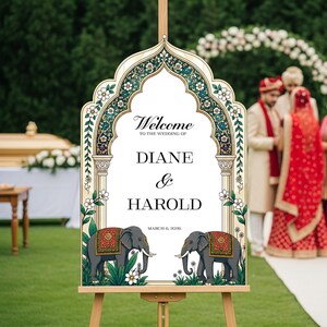 Peut inclure: Un panneau de bienvenue de mariage avec un cadre en arc orn&eacute; de motifs floraux turquoise et dor&eacute;s. Le texte indique Welcome to the wedding of Diane & Harold March 6, 2026. Deux &eacute;l&eacute;phants gris avec des couvertures d&eacute;coratives rouges et dor&eacute;es.