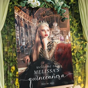 May include: A welcome sign for a quincea&ntilde;era, featuring a photo of a young woman wearing a crown and a sparkly dress. The sign is decorated with a white script font that says "welcome to Melissa's quincea&ntilde;era" and the date "May 20, 2023".
