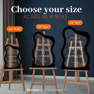 May include: Three irregular wavy-shaped clear acrylic wedding signs on wooden easels. The signs feature white text reading 'WELCOME TO Our Wedding ADELINE and CONNOR 08.09.2026'. Sizes are labeled as 24"x16", 36"x24", and 42"x28" in inches.