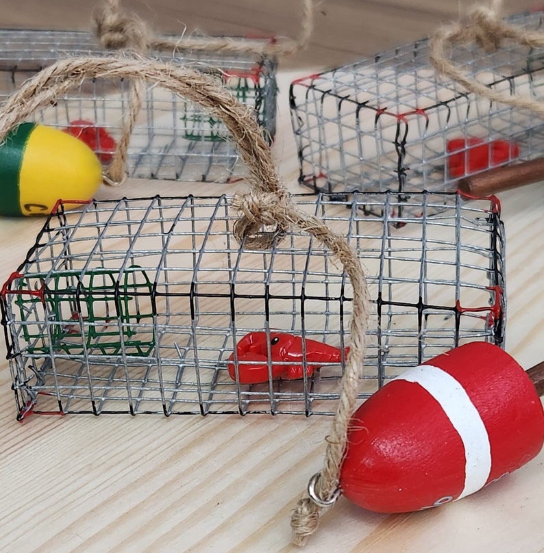 May include: A set of three small wire cages with red lobster and green crab decorations. The cages are hanging from twine and a red and white buoy is attached to the twine.