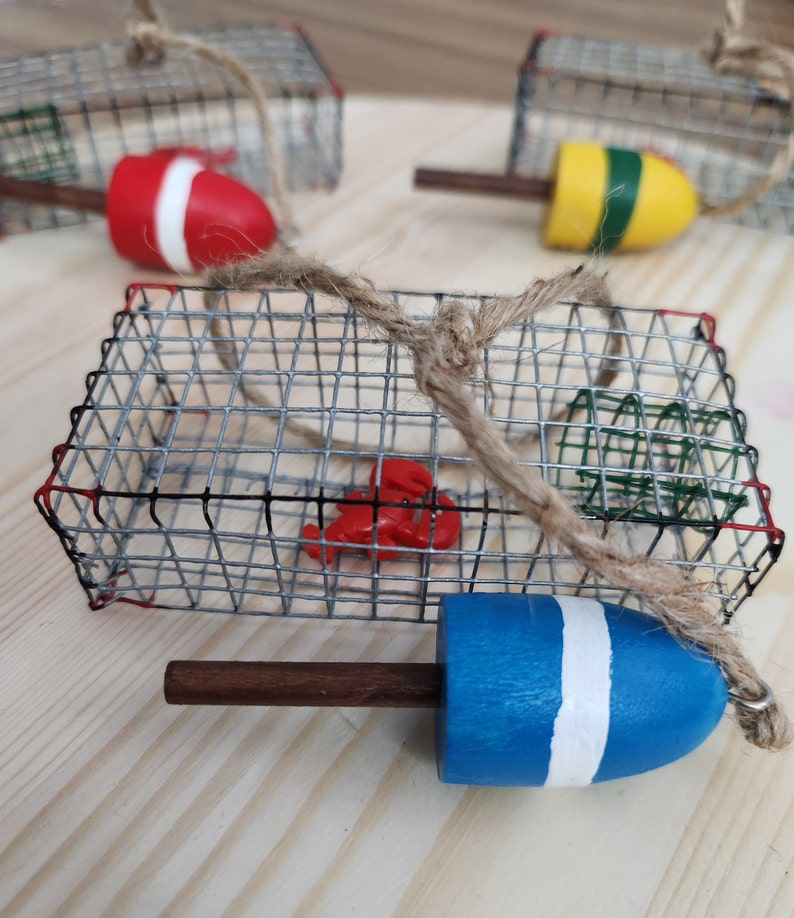 May include: A set of three wire lobster trap ornaments with red, yellow and blue buoys. Each trap is decorated with a small lobster figurine and a piece of twine.