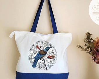 Könnte beinhalten: Weiße Tragetasche mit marineblauen Akzenten und Griffen. Die Tasche zeigt eine kreisförmige Illustration eines blau-braunen Vogels auf einem Ast mit roten und weißen Blüten. Mit Reißverschluss.