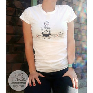 Może przedstawiać: Biała koszulka z czarno-białym rysunkiem osoby siedzącej w pozycji medytacyjnej. Osoba ma krótkie włosy i jest ubrana w czarny strój kąpielowy. Rysunek jest umieszczony centralnie na koszulce.