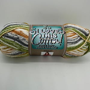 May include: A skein of variegated cotton yarn in shades of green, white, gray, and orange. The yarn is labeled "I Love This Cotton!" with the word "Print" visible. The yarn is a super savings size.
