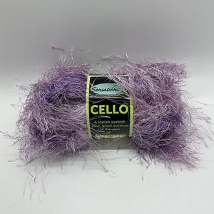 May include: A skein of purple eyelash yarn called "Cello" by Sensations. The label reads "A stylish eyelash yarn, great anytime of the year."