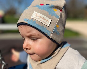 Bij elkaar passende lentehoed en bandana voor pasgeborenen. Katoenen babymutsje met dinosaurusmotief.