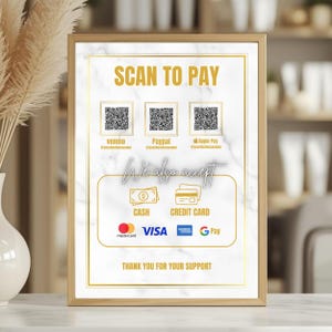 Könnte beinhalten: Ein gerahmtes Schild mit goldenem Rand und marmorähnlichem Hintergrund. Das Schild lautet "SCAN TO PAY" und enthält QR-Codes für Venmo, PayPal und Apple Pay. Es listet auch "CASH" und "CREDIT CARD" als Zahlungsmöglichkeiten auf, mit Logos für Mastercard, Visa, American Express und Google Pay. Der Text "THANK YOU FOR YOUR SUPPORT" steht unten.