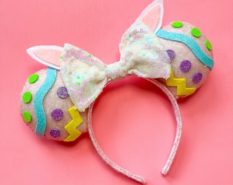 May include: Easter-themed headband with a white bow and two pink, blue, yellow, and purple egg-shaped ears.
