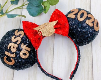 Pode incluir: Orelhas de Minnie Mouse de lantejoulas pretas com um laço vermelho e detalhes de glitter dourado. A orelha esquerda diz "Class of" e a orelha direita diz "2020".