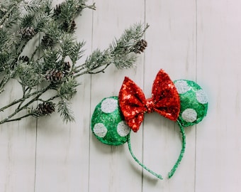 May include: Green and white polka dot Minnie Mouse ears with a red sequined bow. The ears are on a white background.