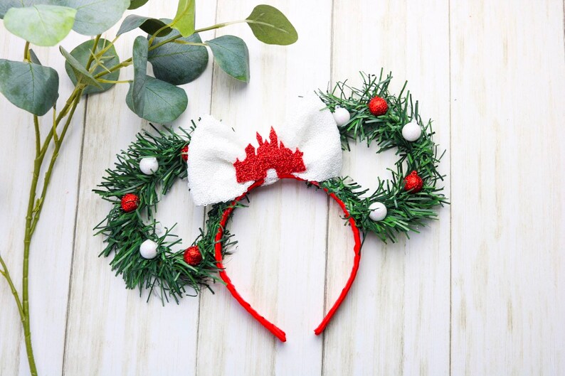 May include: A red headband with a white bow and a red castle silhouette. The headband is decorated with green garland and red and white ornaments.