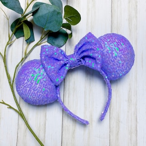 May include: Purple sequined Minnie Mouse ears with a large bow. The ears are made of iridescent sequins and the bow is a large, flat bow.