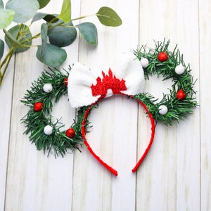 May include: Red and white Christmas themed Minnie Mouse ears with a white bow and a red castle design. The ears are decorated with green garland and red and white ornaments.