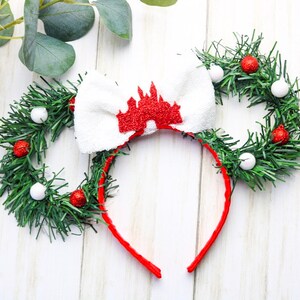 May include: Red and white Christmas themed Minnie Mouse ears with a white bow featuring a red glitter castle design. The ears are made of green garland with red and white ornaments.