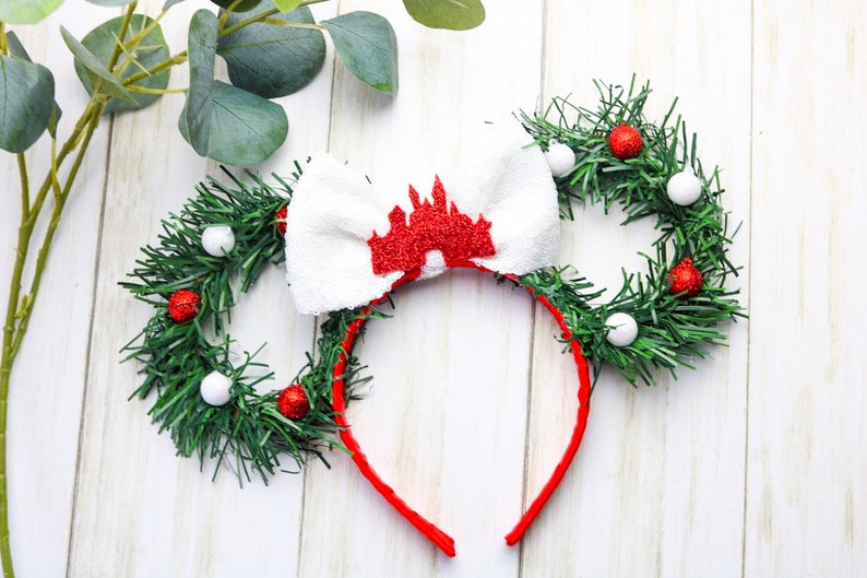 May include: A red headband with a white bow and a red glitter castle design. The headband is decorated with two green wreaths with red and white ornaments.