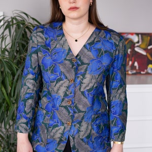May include: A blue and green floral patterned blazer with gold buttons. The blazer has a v-neck and long sleeves.