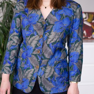May include: A blue and green floral patterned blazer with gold buttons. The blazer has a v-neck and long sleeves.