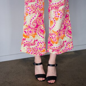 May include: A pair of wide-legged pants with a pink, orange, and white paisley print. The pants are worn with black heeled sandals.