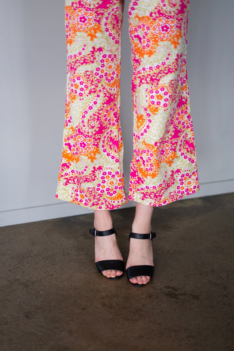May include: A pair of wide-legged pants with a pink, orange, and white paisley print. The pants are worn with black heeled sandals.