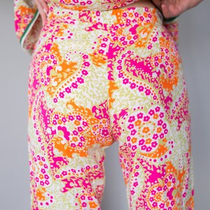 May include: A pair of wide-leg pants with a white background and a paisley pattern in shades of pink, orange, and green.