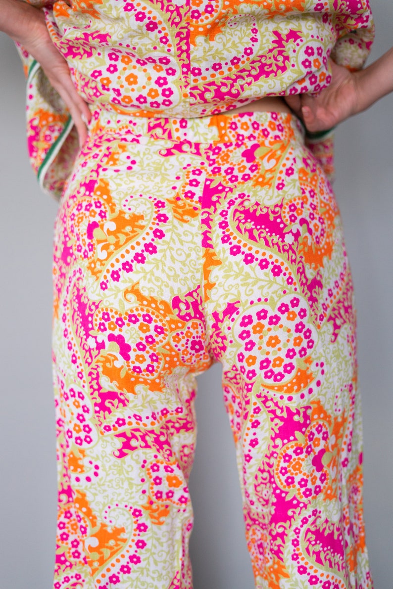 May include: A pair of wide-leg pants with a white background and a paisley pattern in shades of pink, orange, and green.