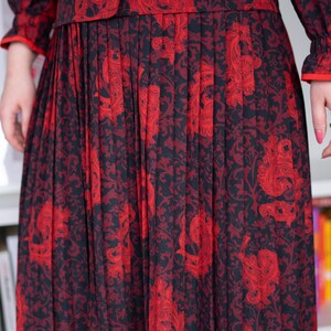 K&ouml;nnte beinhalten: Ein schwarzer und roter Plisseerock mit einem Blumenmuster. Der Rock ist aus einem weichen, flie&szlig;enden Stoff gefertigt und hat ein klassisches, zeitloses Design.