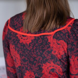 K&ouml;nnte beinhalten: Ein schwarzes und rotes Kleid mit Paisley-Muster. Das Kleid hat einen roten Saum um den Ausschnitt.