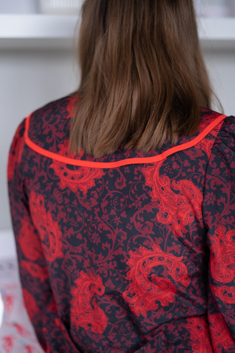 K&ouml;nnte beinhalten: Ein schwarzes und rotes Kleid mit Paisley-Muster. Das Kleid hat einen roten Saum um den Ausschnitt.