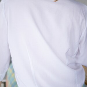 May include: A white long-sleeved button-down shirt with a classic collar. The shirt is made of a smooth, lightweight fabric and has a relaxed fit.
