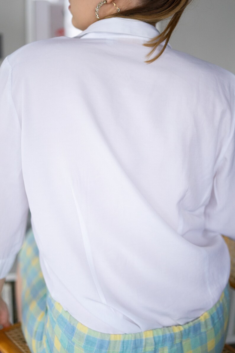 May include: A white long-sleeved button-down shirt with a classic collar. The shirt is made of a smooth, lightweight fabric and has a relaxed fit.