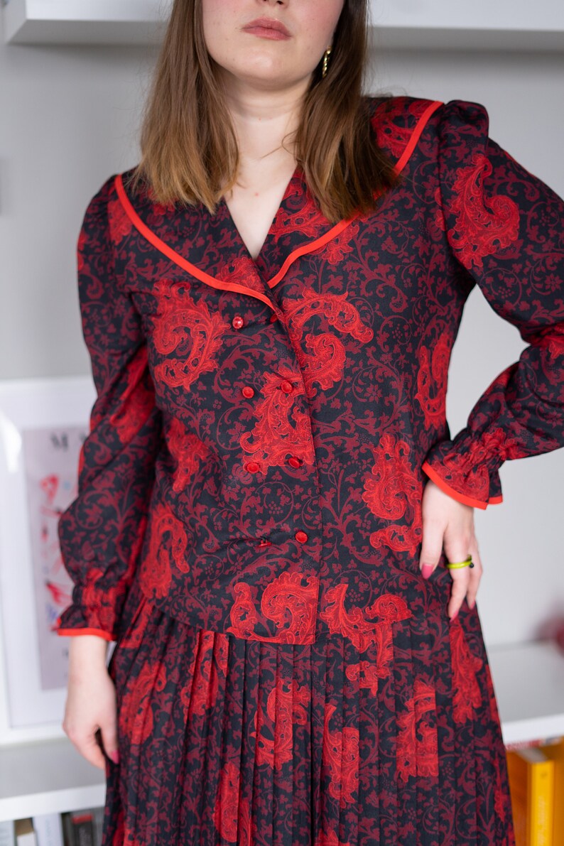 K&ouml;nnte beinhalten: Ein rotes und schwarzes Kleid mit Paisley-Muster, einem Kragen-Oberteil und einem Faltenrock.