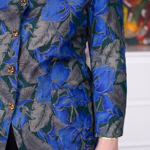 May include: A blue and green floral patterned blazer with gold buttons. The blazer has a v-neck and long sleeves.