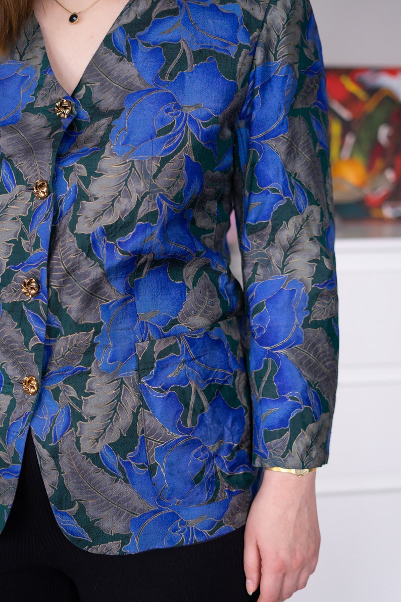 May include: A blue and green floral patterned blazer with gold buttons. The blazer has a v-neck and long sleeves.