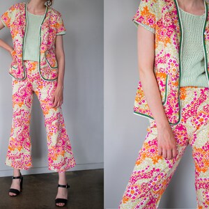 May include: A two-piece outfit with a pink, orange, and white floral pattern. The top is a short-sleeved jacket with a green trim. The pants are wide-legged and also have a green trim.