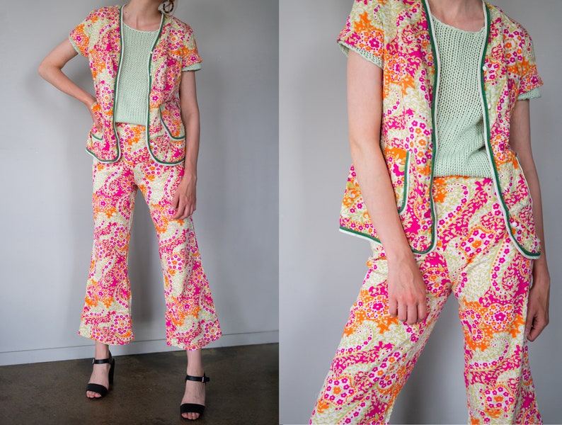 May include: A two-piece outfit with a pink, orange, and white floral pattern. The top is a short-sleeved jacket with a green trim. The pants are wide-legged and also have a green trim.