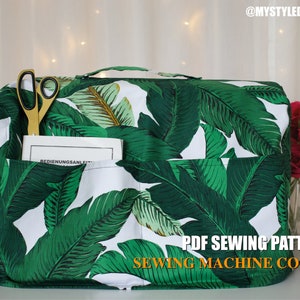 May include: A white sewing machine cover with a green tropical leaf pattern. The cover has two pockets and a handle. The text "PDF Sewing Pattern Sewing Machine Cover" is printed on the front of the cover.