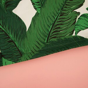 May include: Close-up of a green and white fabric with a banana leaf pattern. The fabric has a stitched edge.
