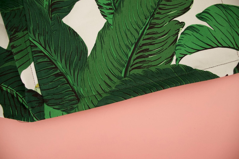 May include: Close-up of a green and white fabric with a banana leaf pattern. The fabric has a stitched edge.
