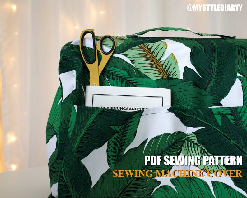 May include: A PDF sewing pattern for a sewing machine cover. The cover is made of white fabric with a green tropical leaf print. The cover has a pocket and a handle. A pair of gold scissors and a book are in the pocket.