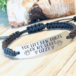 May include: A gray braided bracelet with a silver charm that reads "You left paw prints on my heart ♥ Lizzy ♥" with a paw print on either side of the text.