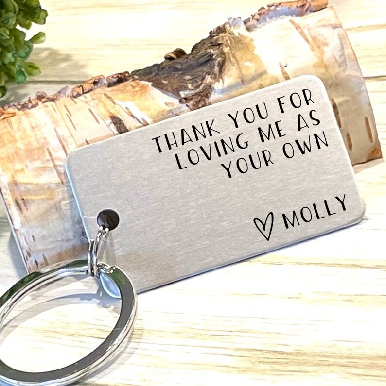 May include: A silver metal keychain tag with the text "THANK YOU FOR LOVING ME AS YOUR OWN" and the name "MOLLY" with a heart symbol. The tag is attached to a silver key ring.