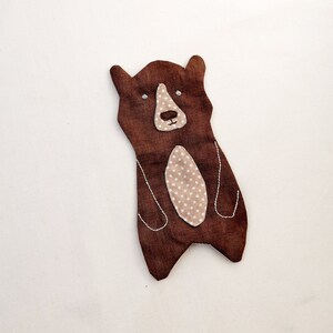 May include: A brown felt bear with a white stitched face and a beige felt belly with white polka dots.