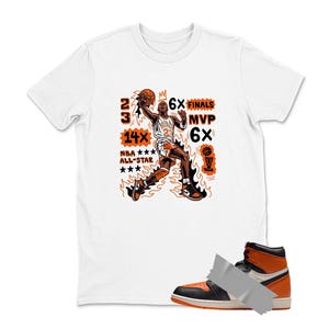 May include: White t-shirt with an orange and black graphic of a basketball player in action, with text that reads "23", "14x NBA All-Star", "6x Finals", and "MVP 6x". A black, white, and orange high-top sneaker is in the foreground.
