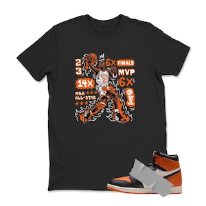 May include: Black t-shirt featuring a basketball player graphic in orange and white, with text including "23", "14X NBA All-Star", and "6X Finals MVP". An orange and black high-top sneaker is taped to the bottom of the shirt.