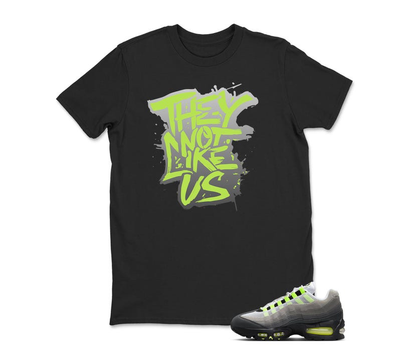 Puede incluir: Camiseta negra con el texto "THEY NOT LIKE US" en verde ne&oacute;n y gris. Un par de zapatillas grises y negras con detalles en verde ne&oacute;n en la parte inferior derecha.