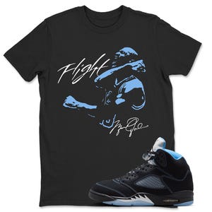 May include: A black short-sleeve t-shirt featuring a light blue graphic of a basketball player in motion with the word Flight and a signature printed in white. Next to the shirt is a black high-top sneaker with light blue accents and a translucent sole.