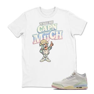 May include: White t-shirt with a cartoon graphic of a character and the text "Y'all Be Capn Too Much." A pair of white, light green, and pink sneakers are in the foreground.